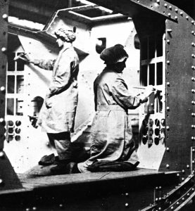 Female factory workers painting the inside of a WW1 British tank with white paint to enhance the small amount of available light inside.